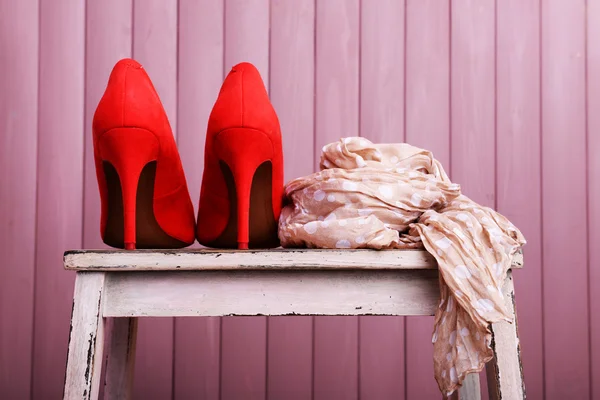 Zapatos de mujer rojos y bufanda en el banco sobre fondo de madera — Foto de Stock