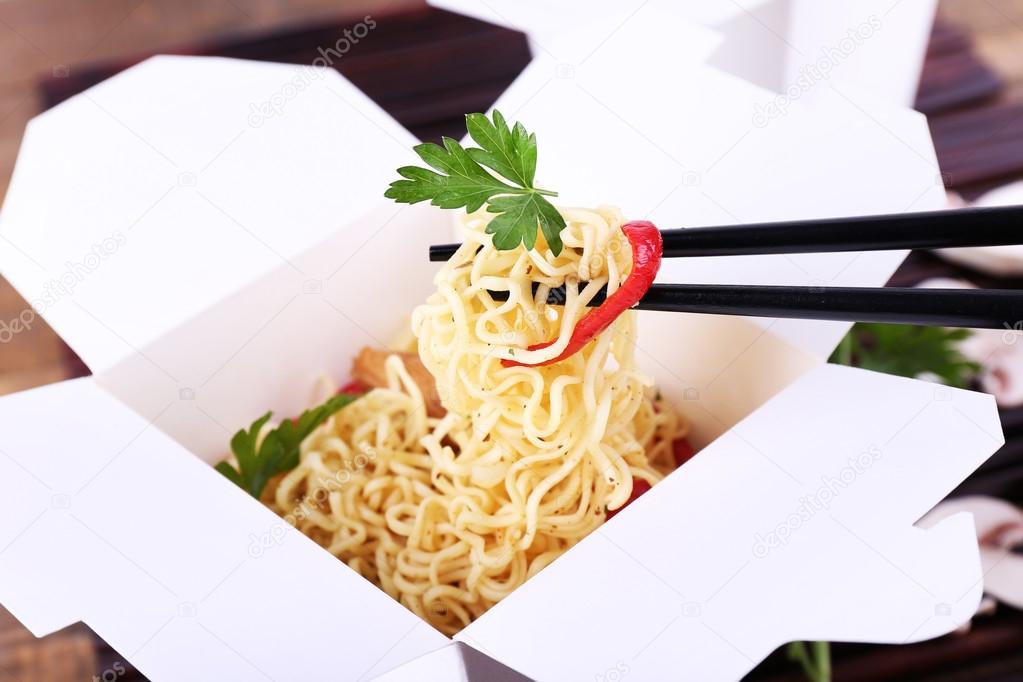 Chinese noodles in takeaway boxes on bamboo mat background