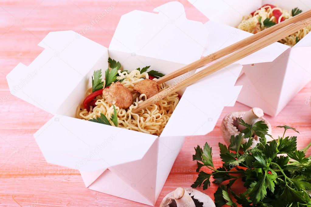 Chinese noodles with meat and pepper in takeaway boxes on pink background