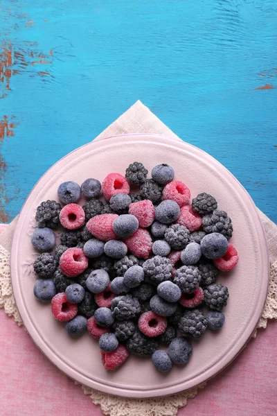 Bayas heladas en plato, sobre fondo de madera de color — Foto de Stock