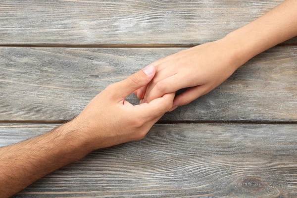 Liebendes Paar hält Händchen aus nächster Nähe auf hölzernem Hintergrund — Stockfoto