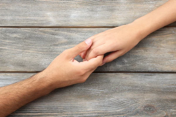 Pareja cariñosa cogida de las manos de cerca sobre fondo de madera —  Fotos de Stock