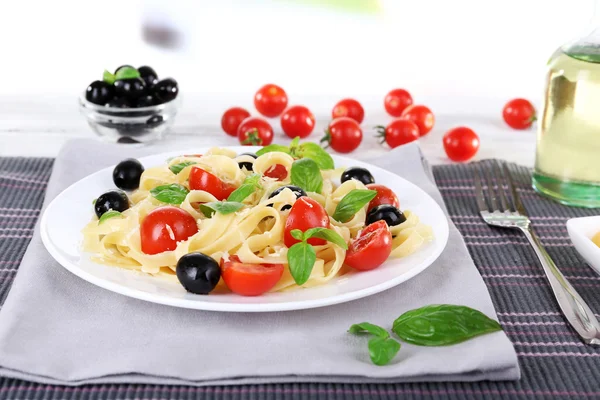Spaghetti con pomodori, olive e foglie di basilico su piatto su tovagliolo su fondo tessuto — Foto Stock