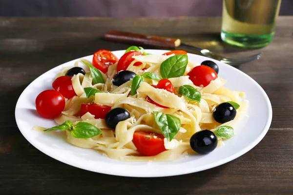 Spaghetti mit Tomaten, Oliven und Basilikumblättern auf Teller auf Holzgrund — Stockfoto