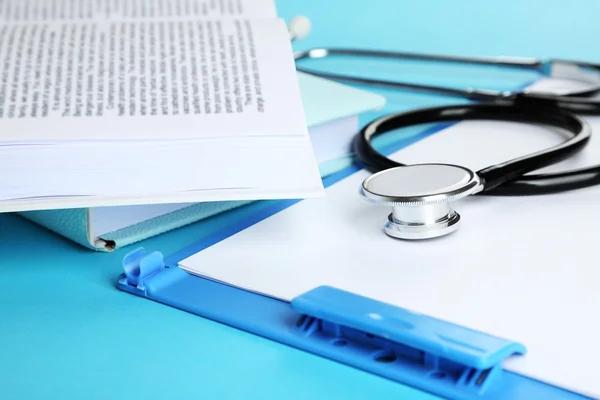 Estetoscópio médico com livros e pasta em fundo azul — Fotografia de Stock