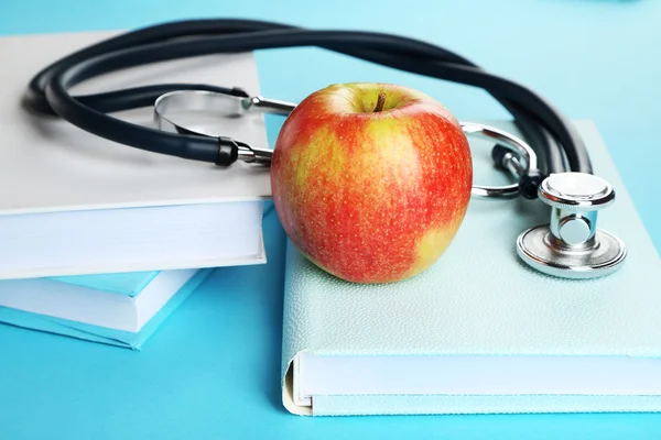 Stetoscopio medico con mela e libri su sfondo blu — Foto Stock