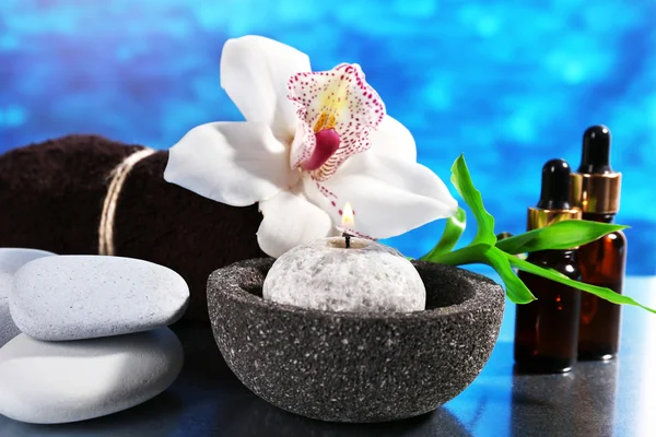 Wellness-Komposition mit Kerze und weißer Orchidee auf Tisch auf blauem Hintergrund — Stockfoto
