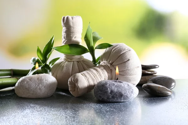 Composición del spa con bolsas de masaje a base de hierbas, vela y bambú sobre la mesa sobre fondo natural — Foto de Stock