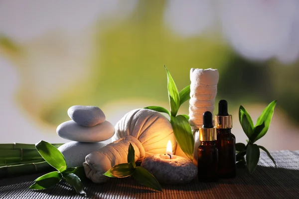 Spa samenstelling met kruiden massage tassen, kaars en bamboe op tafel op natuurlijke achtergrond — Stockfoto