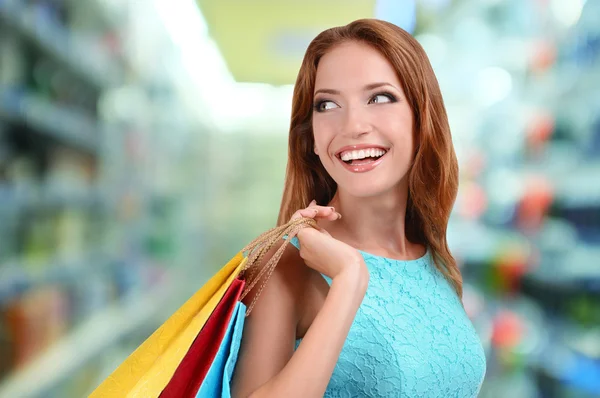 Concetto di shopping. Bella giovane donna con borse della spesa su sfondo negozio — Foto Stock