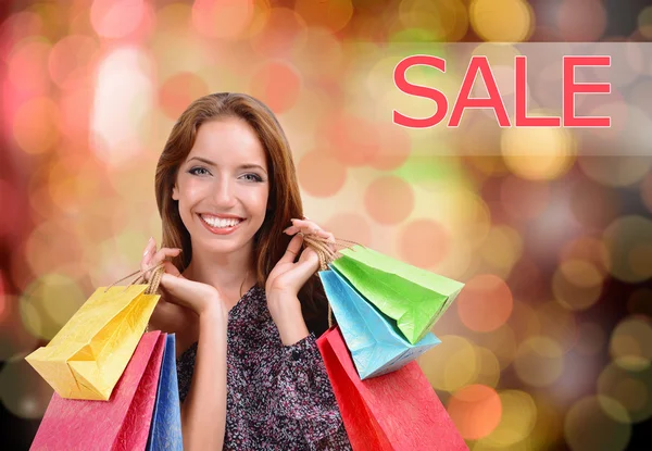 Shopping concept. Beautiful young woman with shopping bags on bright background — Stock Photo, Image