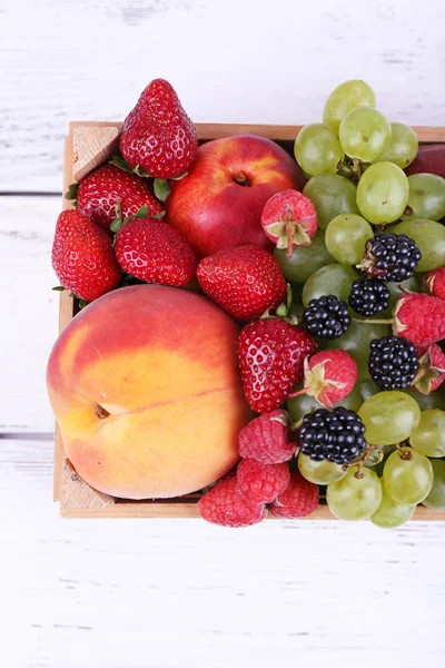 Diferentes bayas y frutas en caja sobre mesa de madera de primer plano —  Fotos de Stock