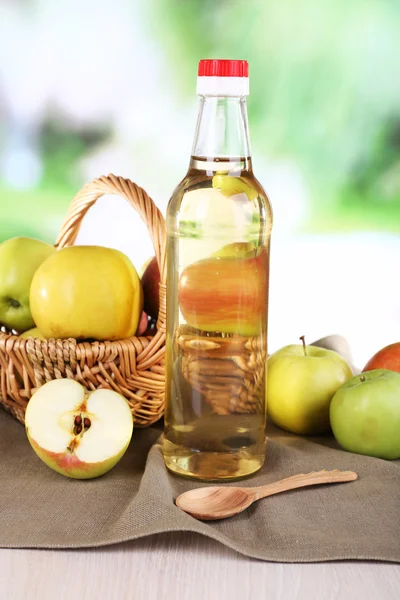 Äppelcidervinäger i glasflaska och mogna färska äpplen, på träbord, på natur bakgrund — Stockfoto