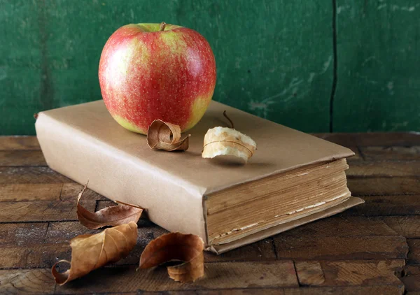 Pomme avec livre et feuilles sèches sur fond en bois — Photo