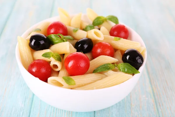 Pasta met tomaten, olijven en basilicum bladeren in kom op houten achtergrond — Stockfoto