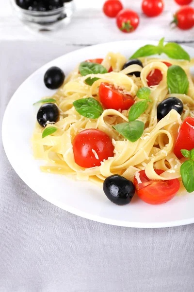 Spaghetti con pomodori, olive e foglie di basilico su piatto su fondo tessuto — Foto Stock