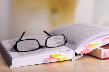 Books with bookmarks and glasses on table on bright background clipart