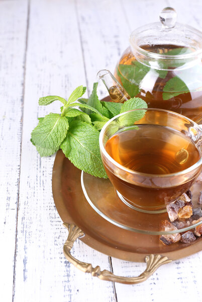 Состав свежего мятного чая в стеклянной чашке и чайник на подносе, на деревянном фоне
