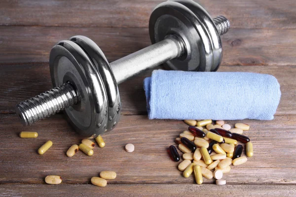 Dumbbell, towel and colorful pills, tablets, on wooden background — Stock Photo, Image