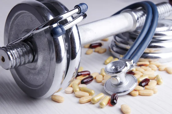 Dumbbell, stethoscope and colorful pills, tablets, on color wooden background — Stock Photo, Image