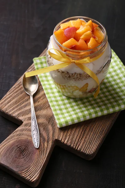 Desayuno saludable yogur con melocotón fresco y muesli servido en frasco de vidrio, sobre fondo de madera — Foto de Stock