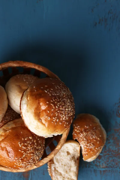 Pães saborosos com gergelim na cesta de vime, na cor de fundo de madeira — Fotografia de Stock