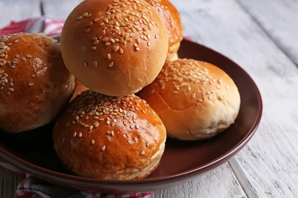 Tasty buns with sesame on plate, on color wooden background — Stock Photo, Image