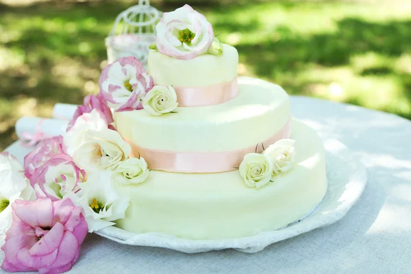 Beautiful wedding cake with flowers on table, outdoors