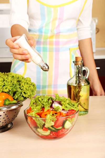 Frau salzt Gemüsesalat in Küche — Stockfoto