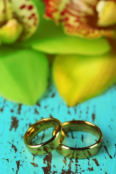 Anneaux de mariage et fleurs d'orchidée, gros plan, sur fond de bois couleur — Photo