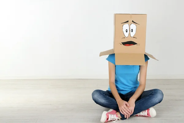 Woman with cardboard box on her head with sad face, near wall — Stock Photo, Image