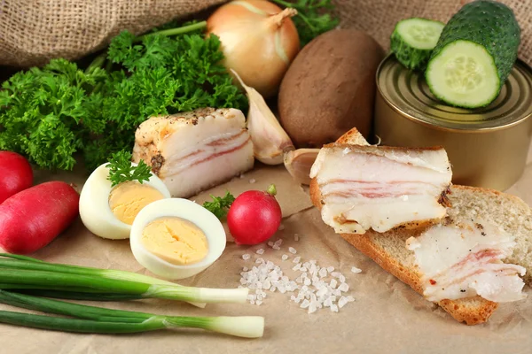 Slanina, čerstvá zelenina, vařené vejce a chléb na papíře, na dřevěném pozadí. Village breakfast concept. — Stock fotografie