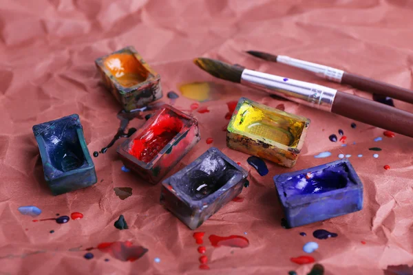 Watercolor paint cubes with brushes and spilled paint on brown paper background — Stock Photo, Image