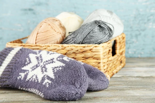 Knitting yarn and mittens in basket, on wooden background — Stock Photo, Image