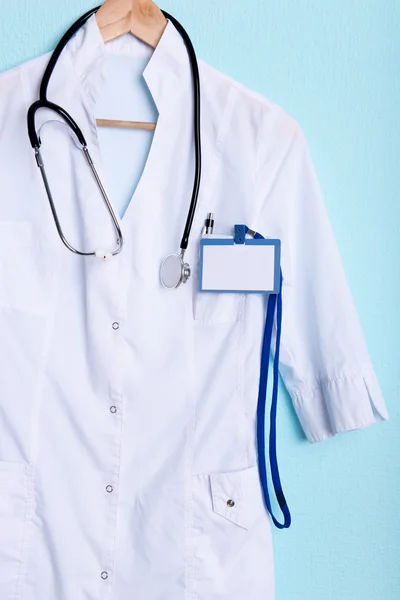 Casaco médico com estetoscópio no cabide no fundo azul — Fotografia de Stock