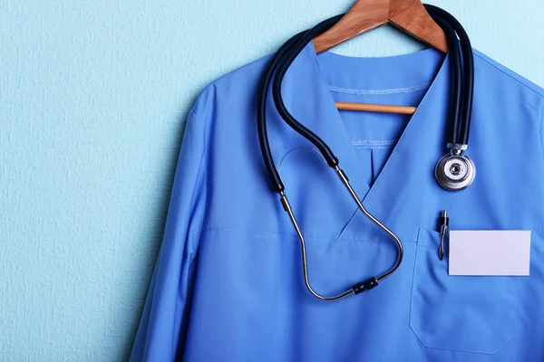 Camisa médica com estetoscópio no cabide no fundo azul — Fotografia de Stock