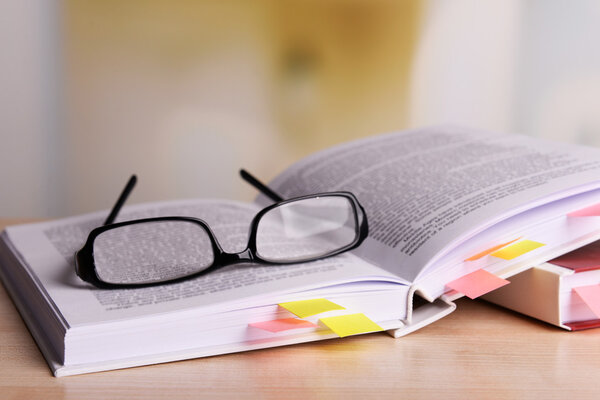 Books with bookmarks and glasses on table on bright background