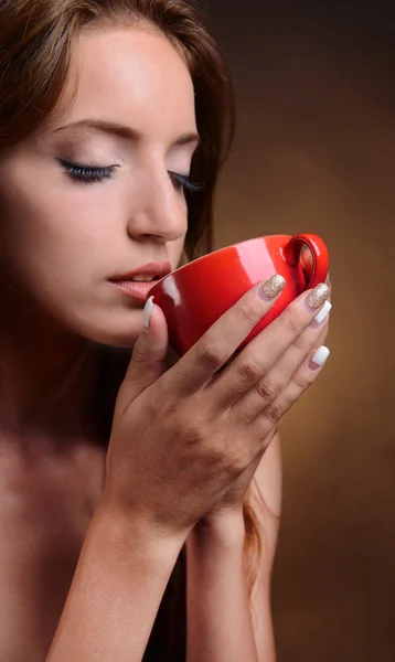 Beautiful young girl with cup of coffee on brown background — Stock Photo, Image
