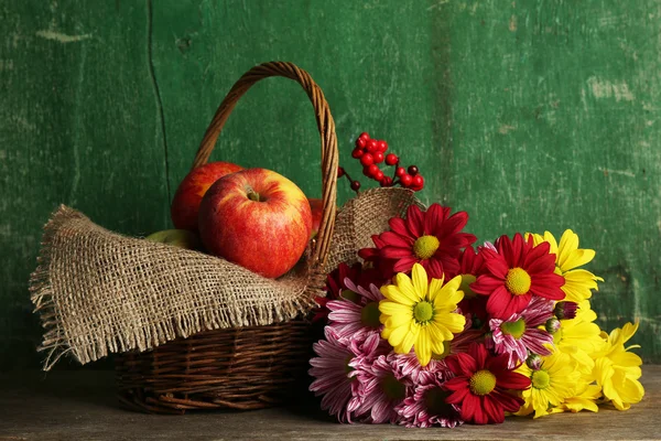 Schöne Chrysantheme mit Äpfeln im Korb auf Holzgrund — Stockfoto