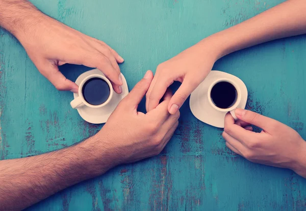 Filiżanki do kawy i trzymając ręce na stole drewniane — Zdjęcie stockowe