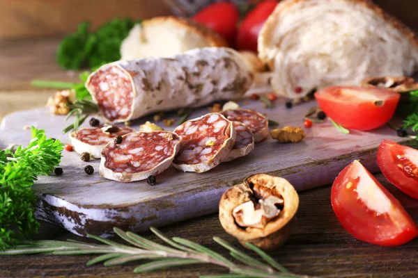 French salami with tomatoes, parsley and bread on cutting board on wooden background — Stock Photo, Image