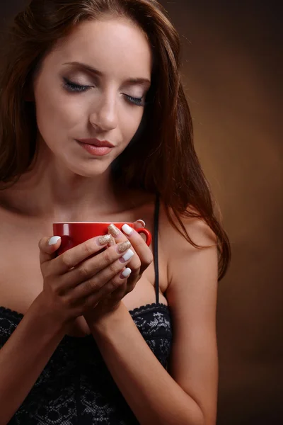 Schöne junge Mädchen mit einer Tasse Kaffee auf braunem Hintergrund — Stockfoto