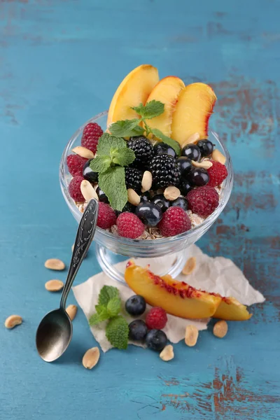 Café da manhã saudável - iogurte com frutas frescas, bagas e muesli servido em tigela de vidro em fundo de madeira colorida — Fotografia de Stock