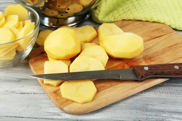 Raw peeled and sliced potatoes  on cutting board, on color wooden background — Stock Photo, Image