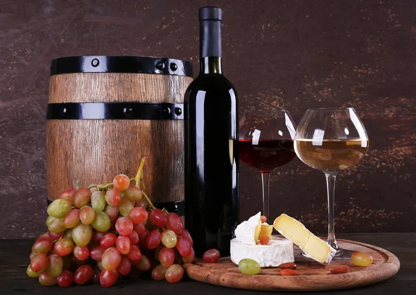 Supper consisting of Camembert cheese, wine and grapes on cutting board and wine barrel on wooden table on brown background — Stock Photo, Image