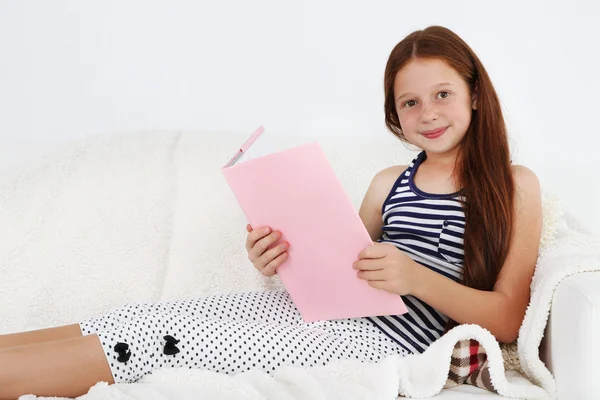 Linda menina leitura livro no sofá no quarto — Fotografia de Stock