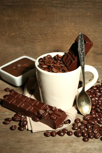 Cup with coffee beans and dark chocolate glaze on wooden background — Stock Photo, Image