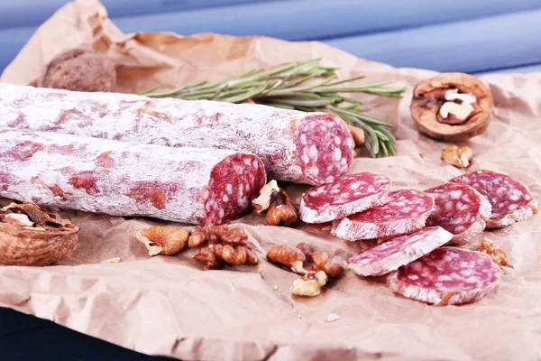 French salami and walnuts on craft paper on dark blue wooden background — Stock Photo, Image