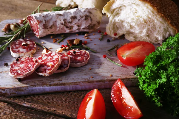 French salami with tomatoes, parsley and bread on cutting board on wooden background — Stock Photo, Image