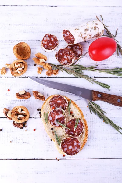 Sandwich with salami, rosemary and walnuts on wooden background — Stock Photo, Image